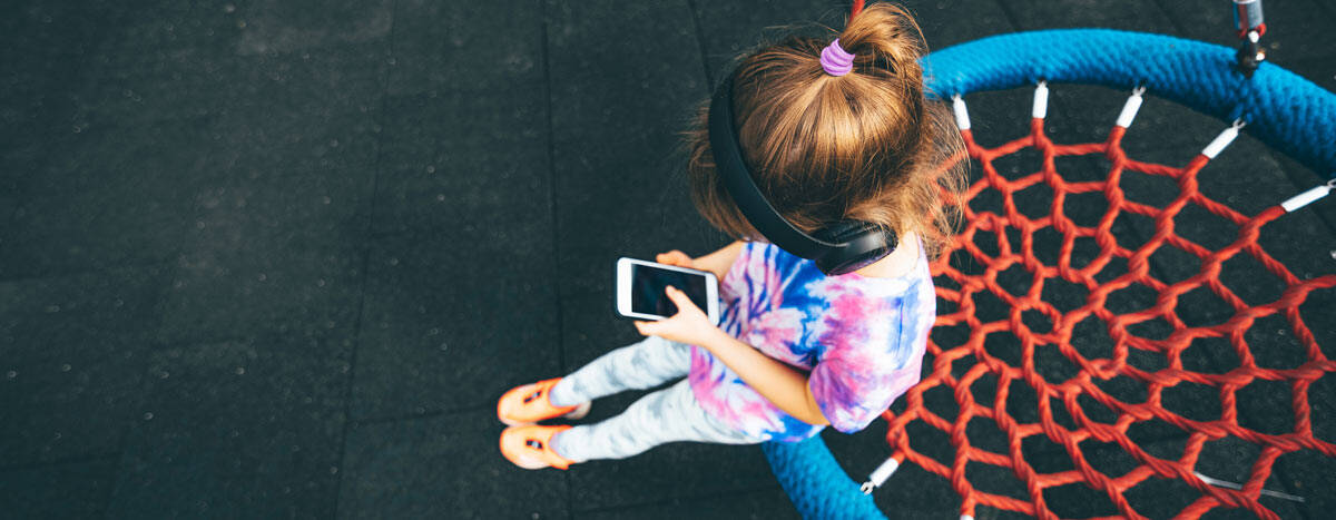 A kid sitting on a net basket and using her phone