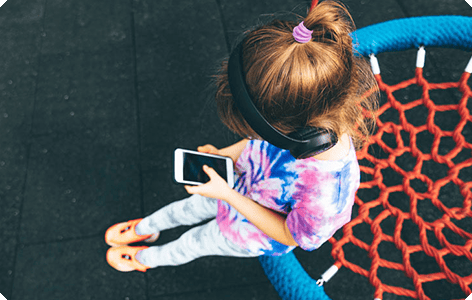 A kid sitting on the rim of a basket net and using her phone