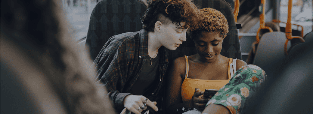 Two teenagers on a bus looking at a phone