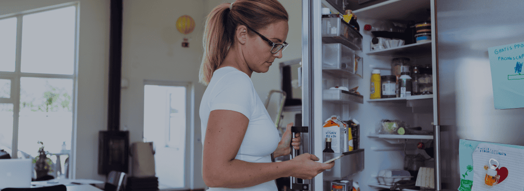 Woman opening fridge looking at her phone