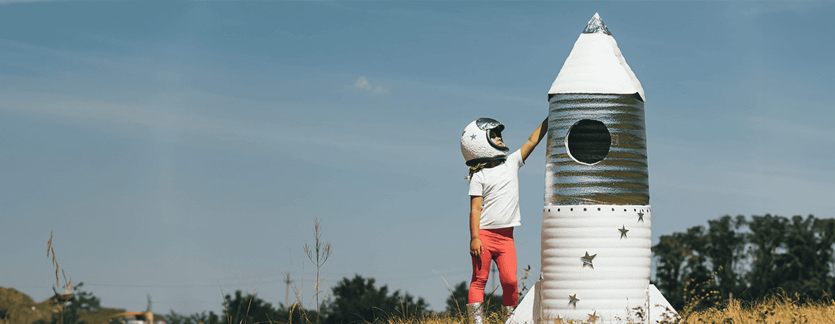 A kid standing next to a paper rocket