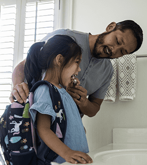 Father helping daughter brush teeth