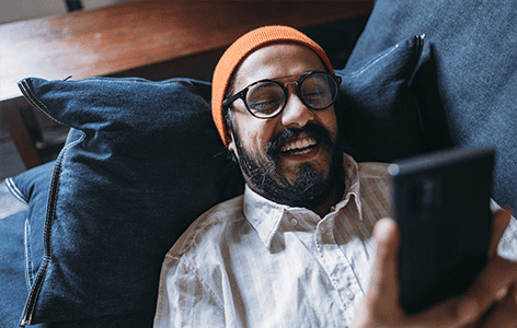 Young man happily looking at smartphone on the couch