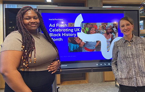Two women smiling and standing in front of a screen with Hall & Partners AD Flash screen
